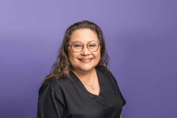 A woman with short light brown hair styled in a bob cut. She has a warm smile and is wearing a purple shirt or jacket
